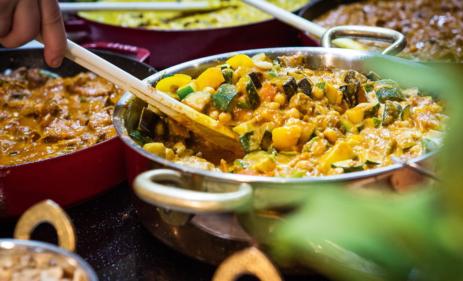 A chef stirring a chickpea curry made for the market kitchen, surrounded by other curries
