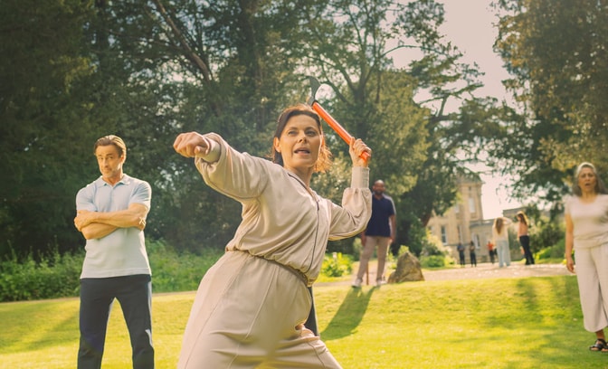 Angie stands firm with an axe ready to throw at the target, Mick looks on in the background with slight concern
