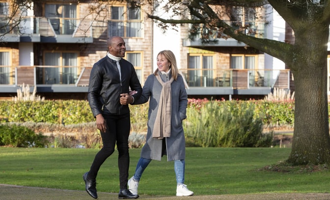 A couple walks hand-in-hand on a grassy path, surrounded by trees and landscaped gardens at Alvaston Hall Hotel