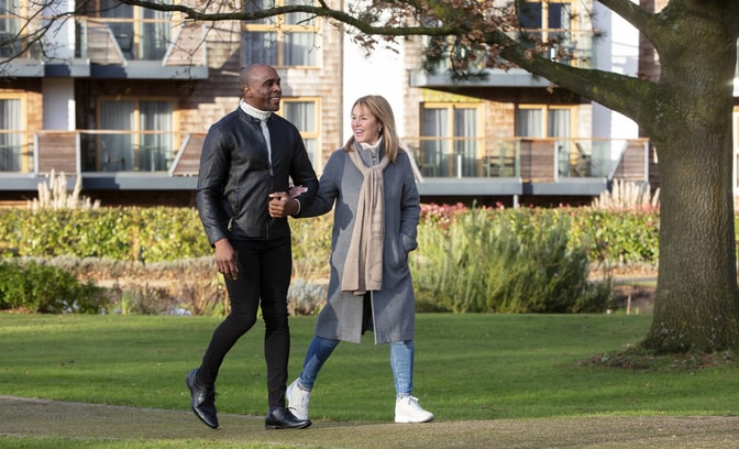 A couple walks hand-in-hand on a grassy path, surrounded by trees and landscaped gardens at Alvaston Hall Hotel