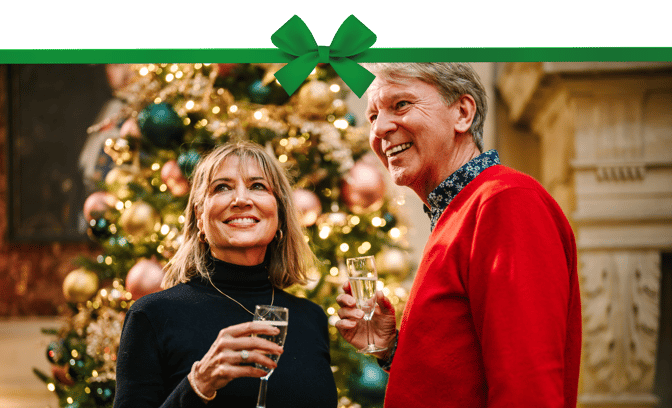Two people with glasses of prosecco, smiling in front of a christmas tree