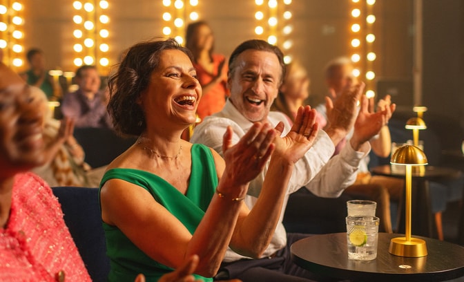 A lady claps in the audience of an intimate auditorium as she watches a performance on stage