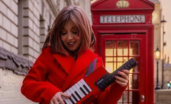 Philippa Healey playing a keytar in front of a telephone box