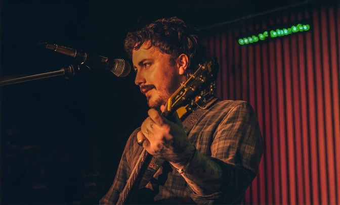 Joe Keeley - holding a guitar and singing into a microphone