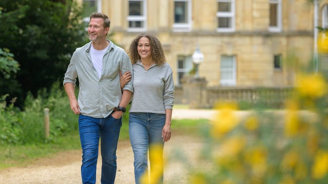 Two hotel guests strolling through the grounds of a hotel with bright yellow flowers in the foreground