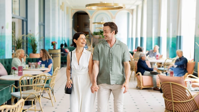 Two guests wander through the Orangery hand in hand and smiling at eachother at Heythrop Park