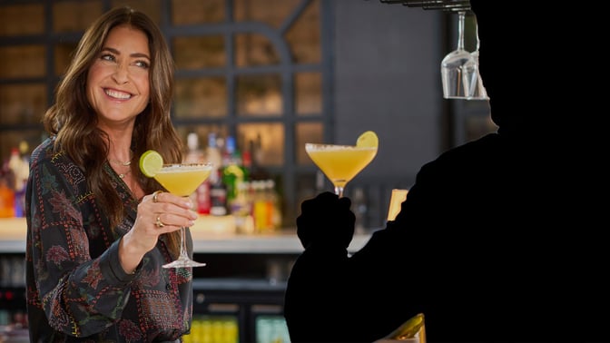Lisa Snowdon hands a cocktail to a mystery guest