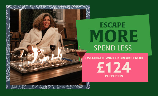 A woman in a cozy white robe relaxes by a fire table, enjoying drinks while promoting winter breaks starting at £124 per person.