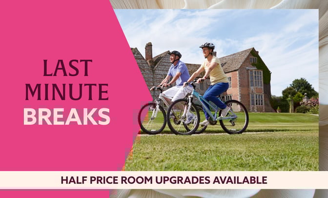 Two cyclists enjoy a sunny day on manicured grass in front of a historic building, promoting last minute breaks and room upgrades.