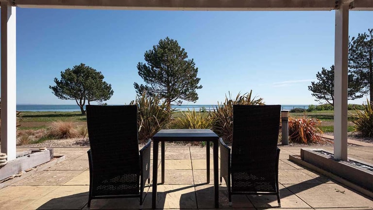 Private patio with outdoor seating and views across landscaped grounds to the coast and sea.