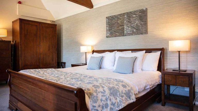 Royal bedroom with a king-size wooden sleigh bed, bedside tables, and exposed timber beams.