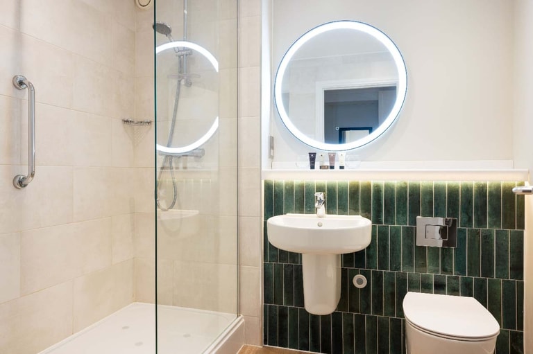 Modern bathroom with a walk-in shower, illuminated round mirror, pedestal sink, and WC.