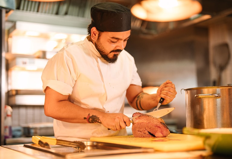 Chef carving freshly roasted meat in an open kitchen