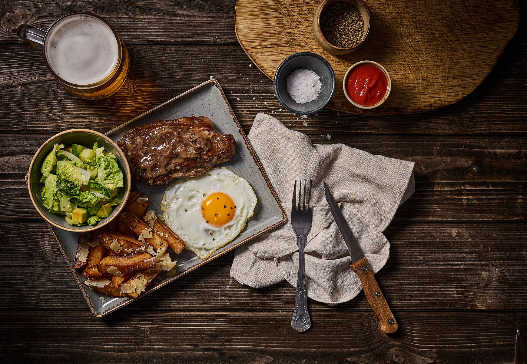 aerial view of steak, chips, fried egg and salad with some condiments and a pint of beer
