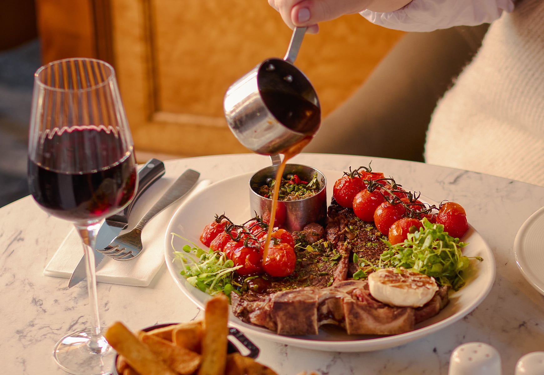 T bone sharer steak plate with graving being poured over and a glass of red wine