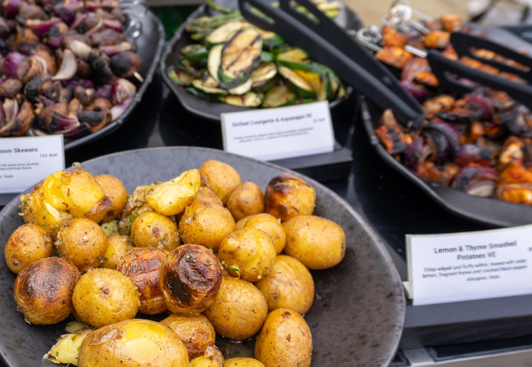 Selection of Big Green Egg dishes including roasted potatoes, grilled courgette, mushrooms and skewers displayed on a buffet counter.