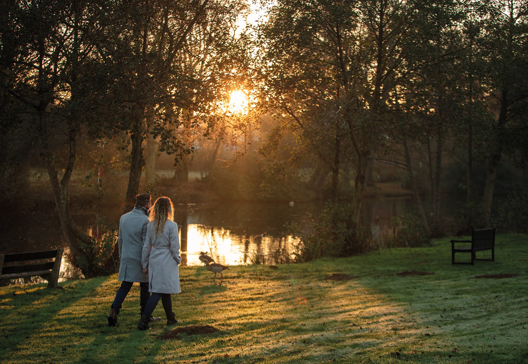 Two people walking hand in hand by a lake at sunset