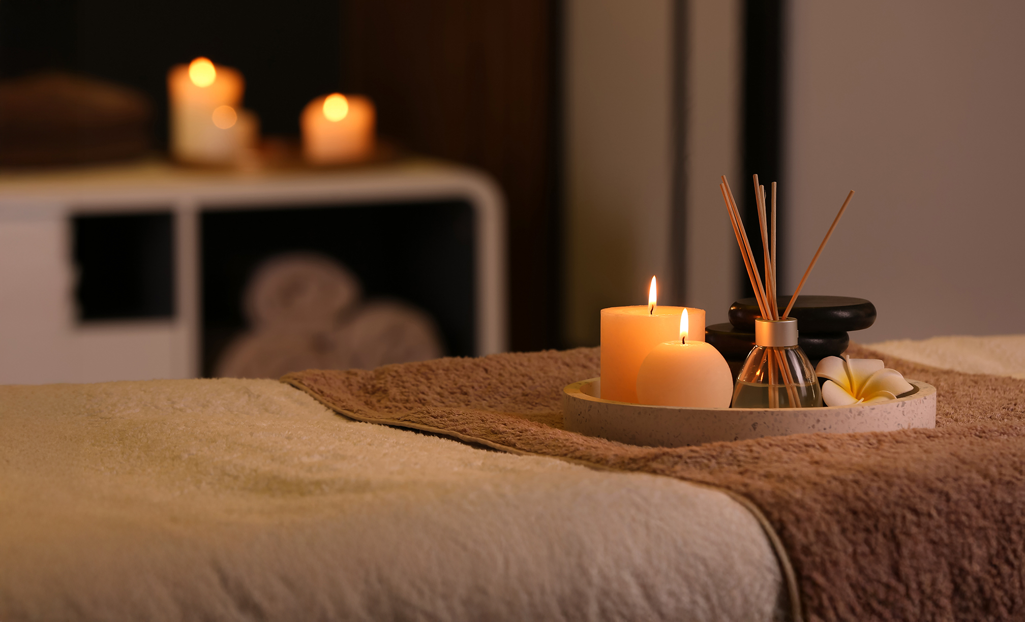 A spa treatment room featuring candles and a soft towel on a treatment bed