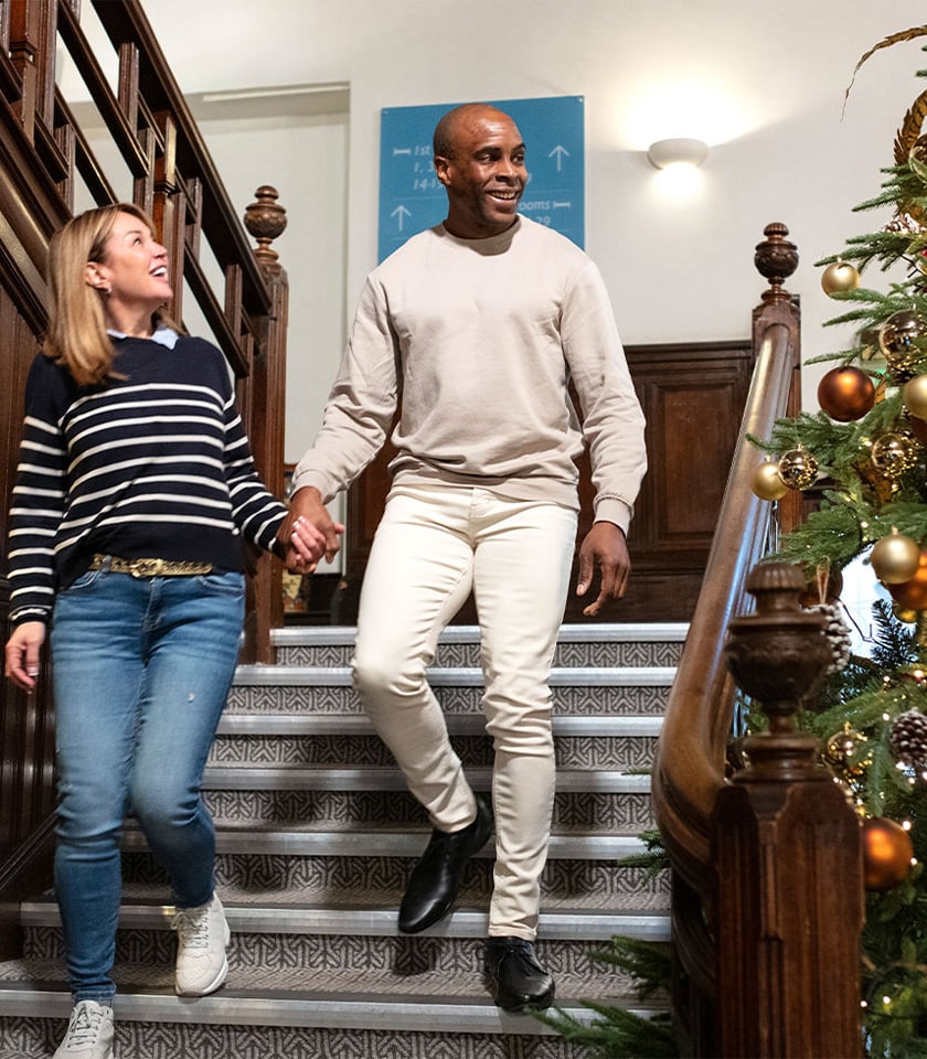 A couple walks down stairs next to a vibrant Christmas tree, capturing the essence of a joyful and festive atmosphere.