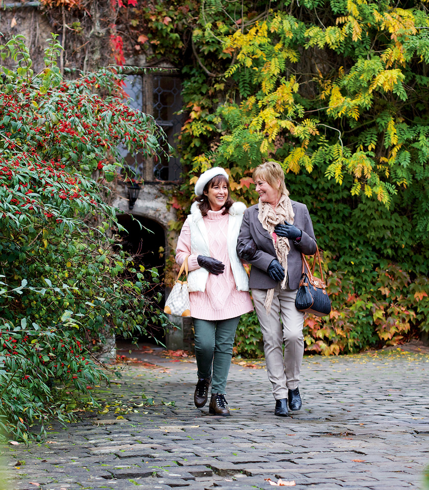 Two women stroll together along a charming cobblestone path, enjoying their time outdoors.