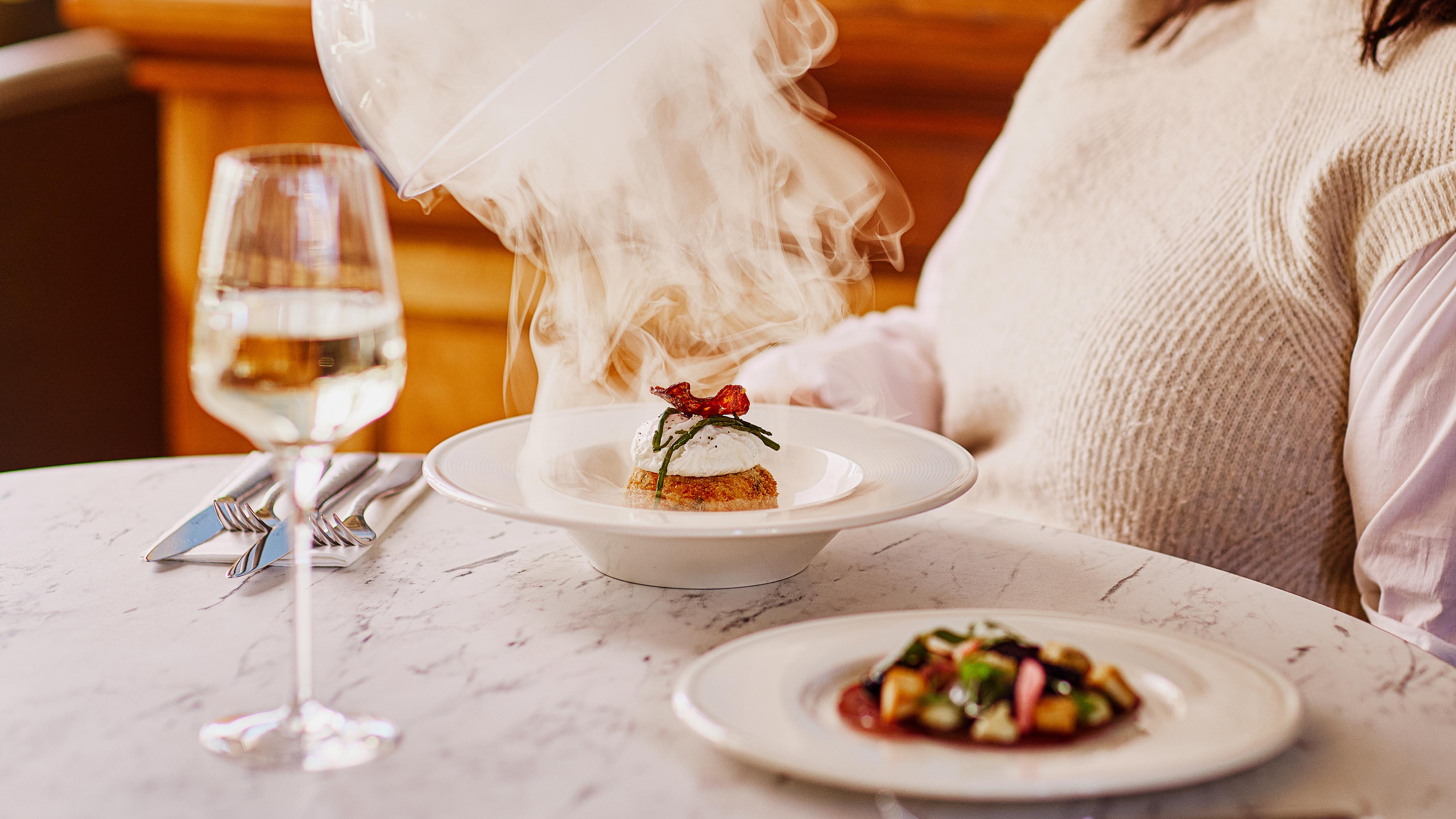 Close up of a smoked haddock fishcake and a glass of wine being served to a guest